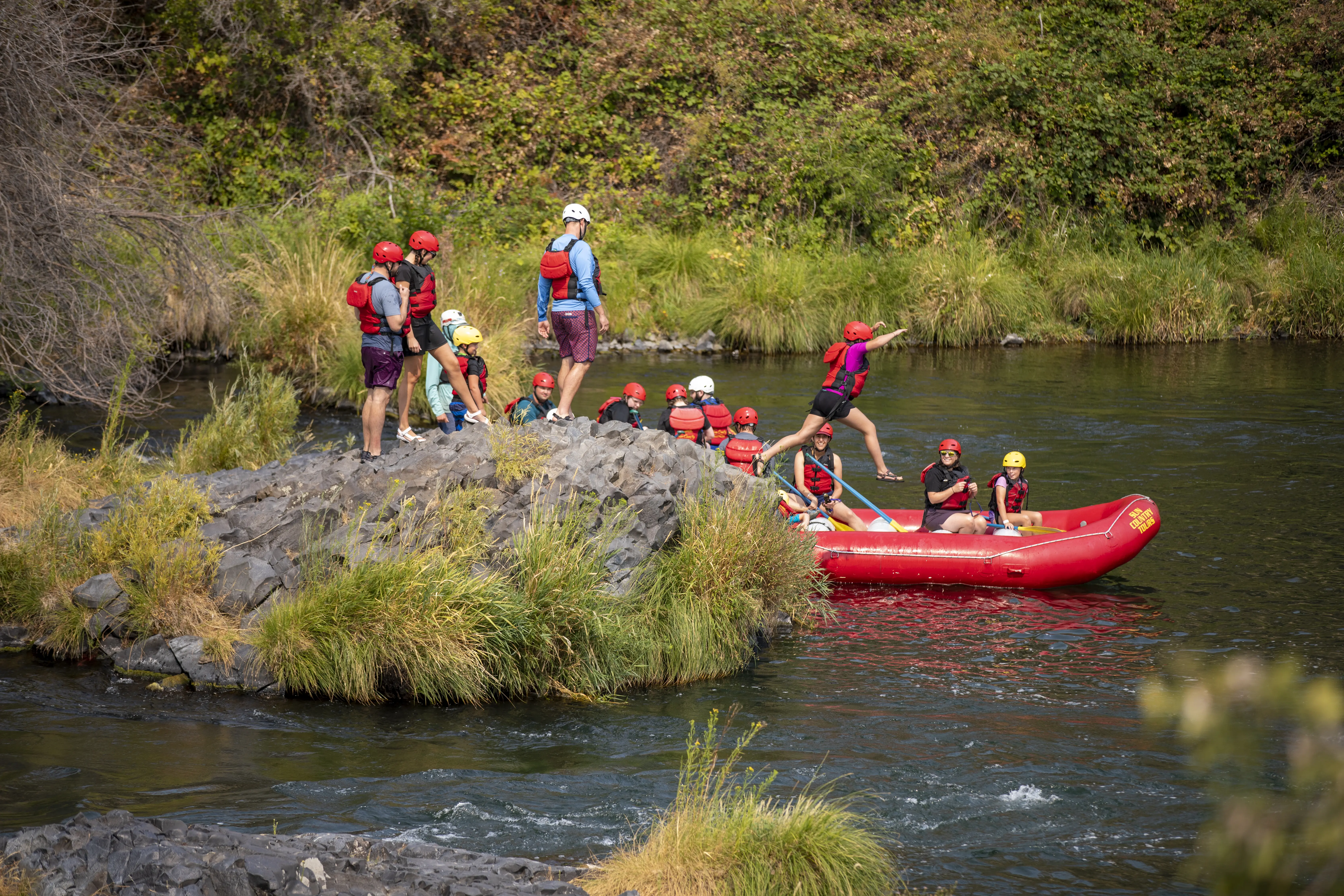 Group of Sun Country Tours rafters leaping off a rock into the river, their rafts waiting nearby, exemplifying the joy and adventure of rafting trips.