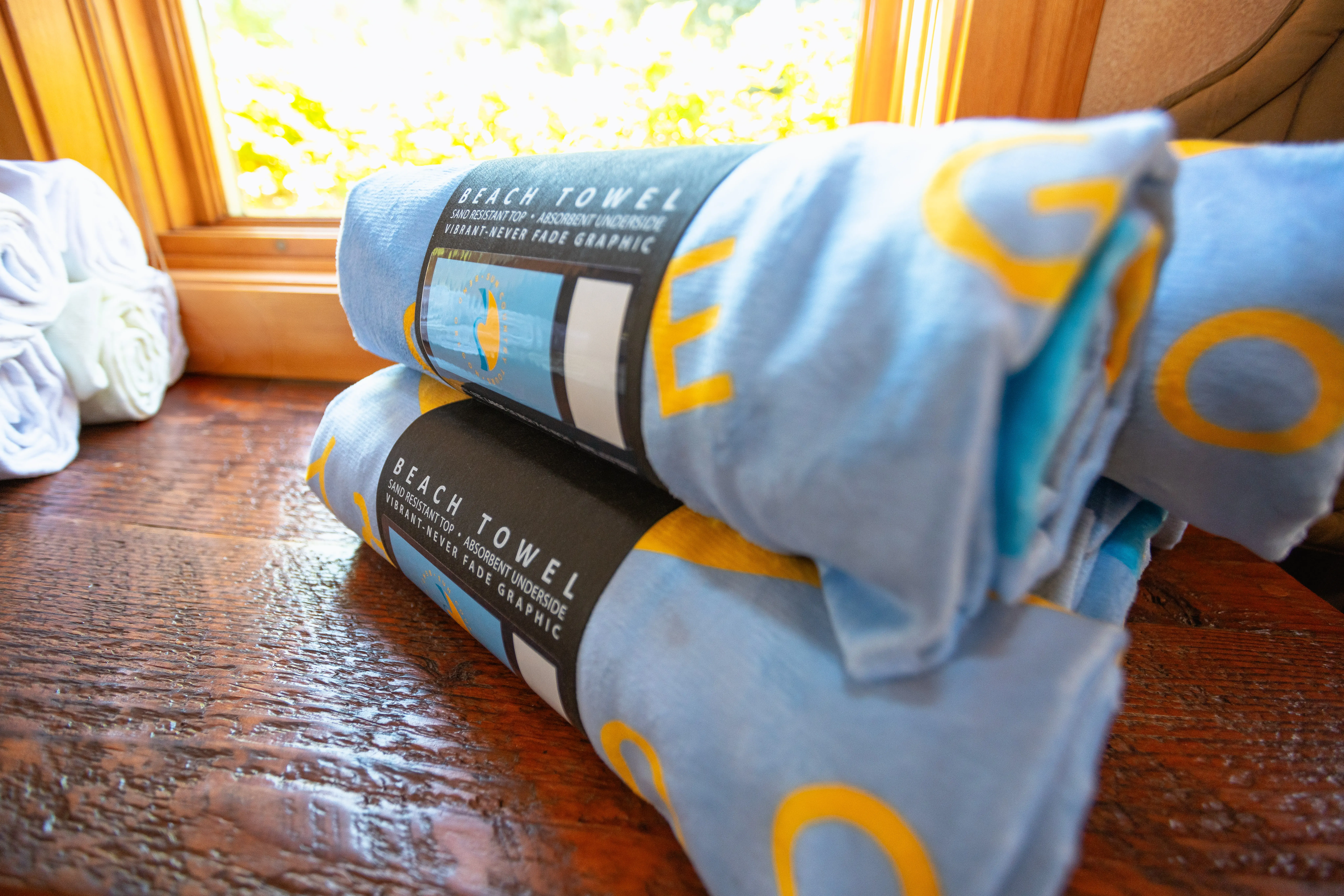 Rolled beach towels with vibrant graphics displayed on a wooden surface, perfect for rafting and outdoor activities at Sun Country Tours.